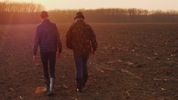 夕阳西下，中年农民带着儿子穿过田野。家庭农场概念 — 图库视频影像