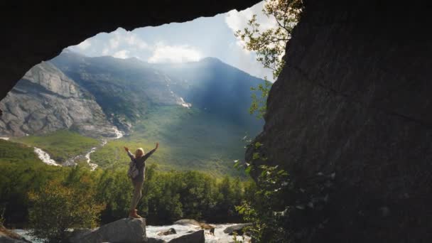 The traveler joyfully raises his hands up, enjoys the incredible nature around. View through the arch in the rocks, the sun shines in the frame. The dream of a tourist — Stock Video