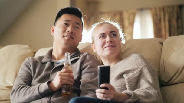 Junge multiethnische Familie vor dem Fernseher, Mann trinkt ein Getränk aus einer Flasche — Stockvideo