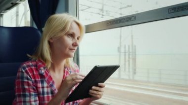 Genç bir kadın bir trende yolculuk ediyor. Pencerenin kenarında oturur, dijital tablet kullanır