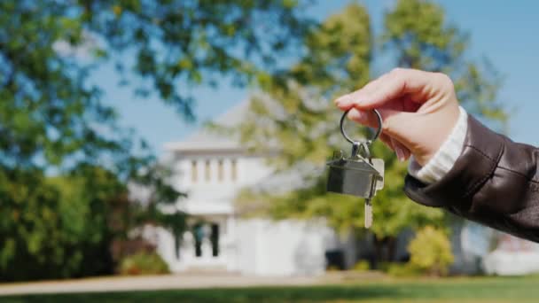家の鍵を渡して米国郊外からの典型的な家の背景に。住宅コンセプトの購入と賃貸 — ストック動画