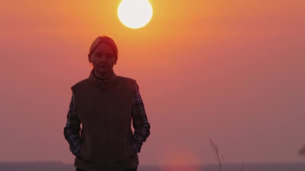 A woman walks toward the camera, a large red sun shines from behind — Stock Video