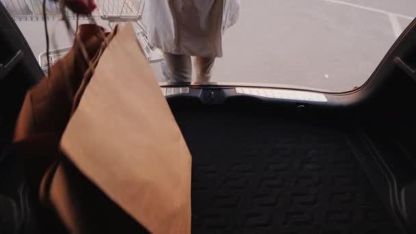 Pohled z auta: žena staví nákupní tašky do kufru auta.