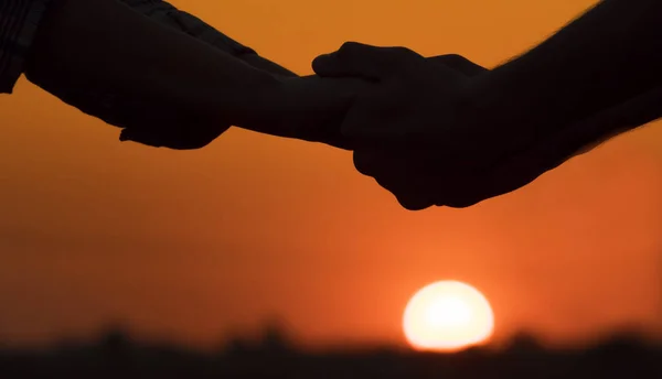 Büyük bir batan güneşin arka planda genç bir çiftin elleri — Stok fotoğraf