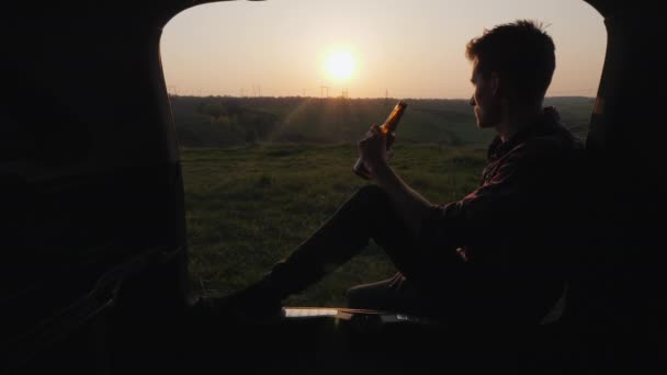 Nastolatek siedzi w bagażniku samochodu i pije piwo z butelki — Wideo stockowe