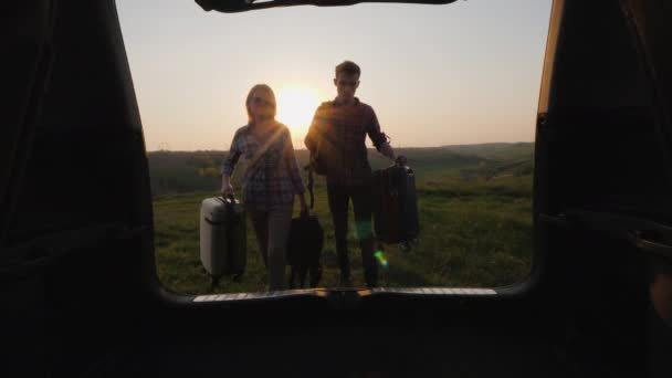 Пара туристов загружает сумки в багажник автомобиля — стоковое видео