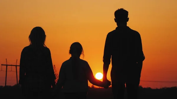 Familie van drie bewonderen de oranje zonsondergang over de stad, achteraanzicht — Stockfoto