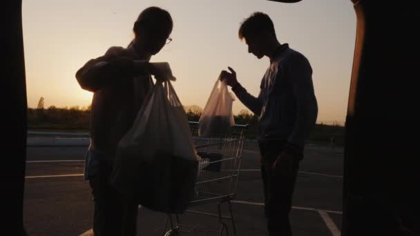 한 남자와 한 여자가 자동차 트렁크에 있는 트롤리에서 물건을 내리고 있다. 음식 구매 — 비디오