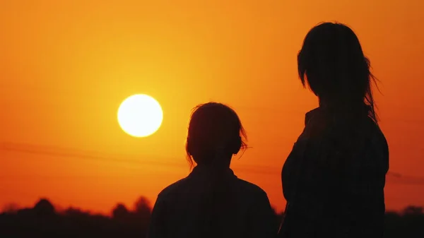 Mãe e filha olham para o lindo pôr do sol sobre a cidade e o céu laranja juntos — Fotografia de Stock