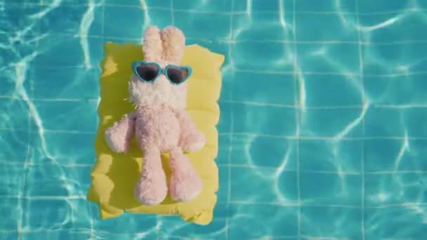 Een pluche Bunny zweeft op een gele opblaasbare matras in het zwembad. Rusten met kinderen concept — Stockvideo