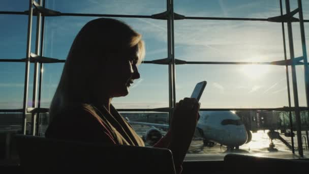 Üzleti nő várja, hogy a fedélzeten járat a repülőtéri terminál, egy okostelefon — Stock videók