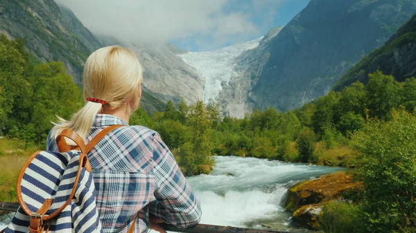 Een vrouwelijke reiziger kijkt de prachtige bergen en de gletsjer op de top. Briksdal gletsjer in Noorwegen — Stockfoto