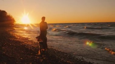 Genç bir kadın gün batımında Ontario Gölü kıyısında bir köpek ile yürüyor. Rüzgarlı hava, güzel gün batımı
