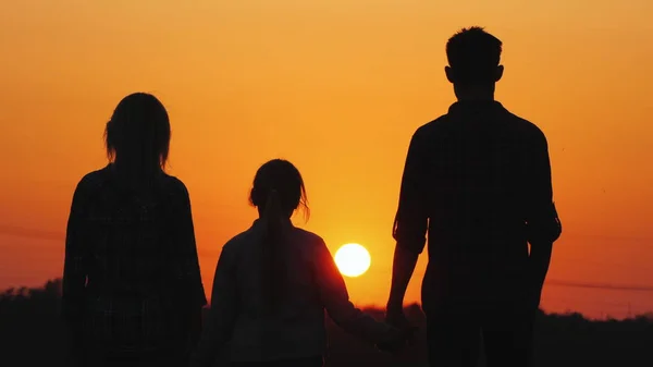 Een gezin met een kind kijkt naar de ondergaande zon boven de stad. Een goede tijd samen. — Stockfoto