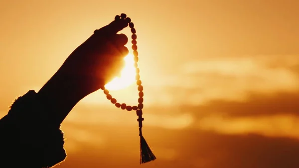 Main tient le chapelet contre le ciel et le soleil couchant, prière sincère et méditation — Photo