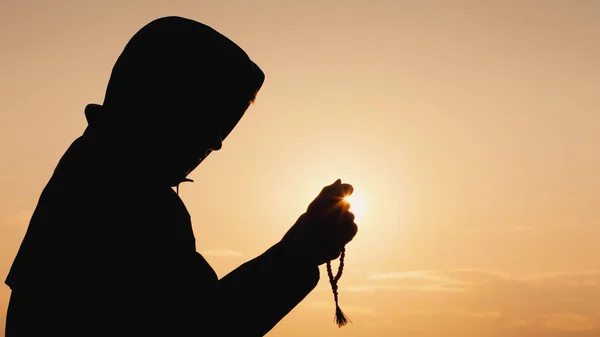 Un homme en robe médite au coucher du soleil, passe par le chapelet dans ses mains — Photo