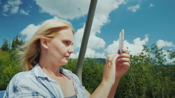Mujer joven activa en vacaciones de verano en las montañas. Va en un ascensor, toma fotos de hermosas vistas de las montañas — Vídeo de stock