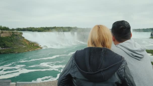 Активная супружеская пара проводит выходные на Ниагарском водопаде, глядя вдаль на каскад водопадов — стоковое видео