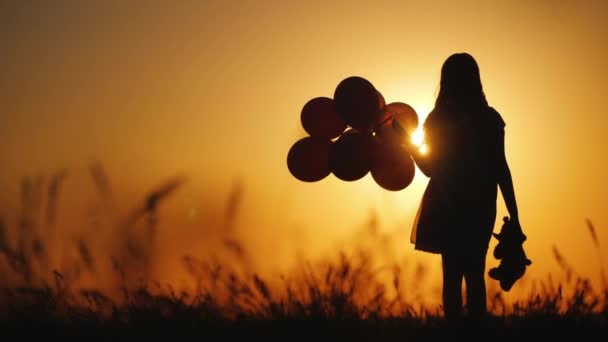 Sziluettje egy lány léggömbök és egy mackó. Megéri a naplementét. Búcsú a gyermekkori koncepció — Stock videók