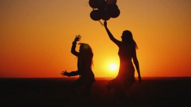 Anne ve kızı gün batımında eğleniyor, dans ediyor ve balonları tutuyorlar.