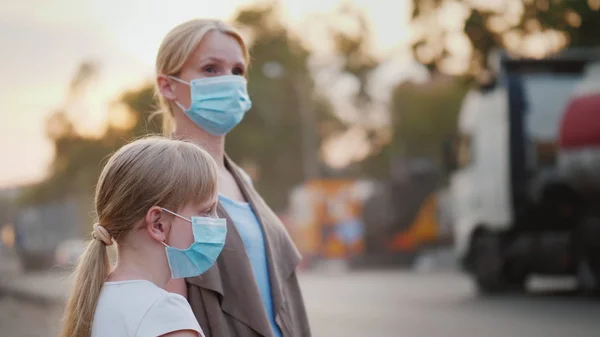 Kobieta z dzieckiem w maskach ochronnych stoi w pobliżu brudnej, zakurzonych drogach w mieście — Zdjęcie stockowe