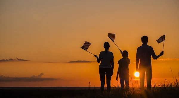 Família com criança acenando bandeiras americanas ao pôr do sol, visão traseira — Fotografia de Stock