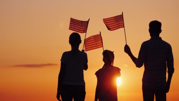 Famille heureuse avec enfant agitant des drapeaux américains au coucher du soleil, vue arrière — Video