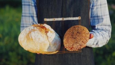 Bir fırıncı iki somun açık ve koyu ekmek tutar.