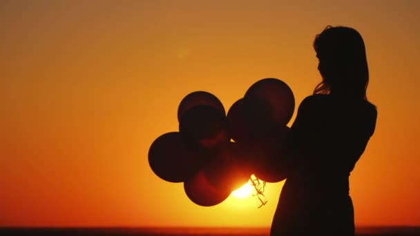 Силует молодої жінки з повітряними кулями на заході сонця — стокове відео