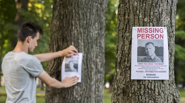 A young man puts up ads for a missing person in the park — Stock Photo, Image