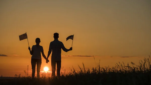 Hombre y mujer con banderas americanas en sus manos están mirando al sol naciente — Foto de Stock