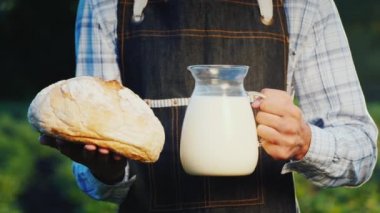 Bir adam, elinde süt ve bir somun ekmekle cam sürahi tutan bir çiftçidir.