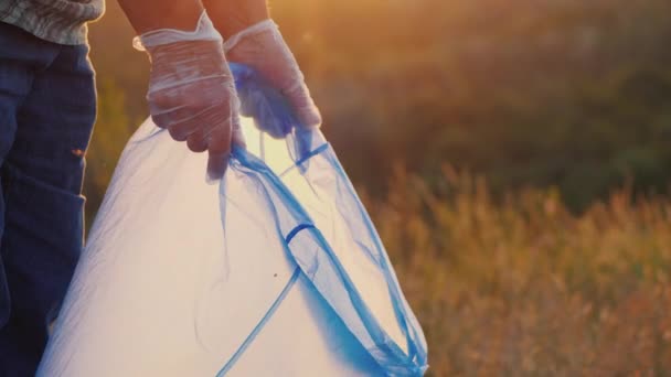 Gloved mensen opruimen in de natuur, zet flessen in een zak — Stockvideo