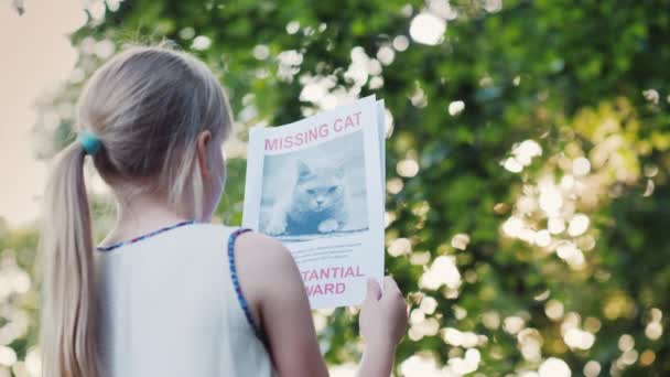 Het kind is op zoek naar een verloren huisdier. Staat in het park met de aankondiging van het verlies van een kat — Stockvideo