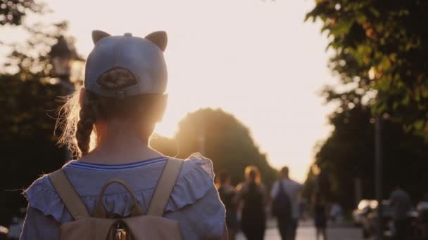 Een meisje met een rugzak is in een stadspark, voorbijgangers gaan door — Stockvideo