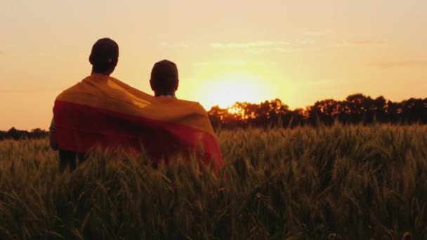 Dois homens com a bandeira da Alemanha atrás dos ombros estão num lugar pitoresco num campo de trigo. — Vídeo de Stock