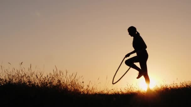 Silhouette egy nő-jumping át a kötelet naplementekor — Stock videók