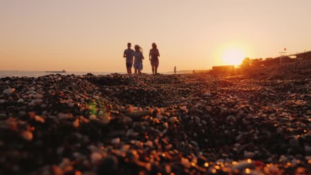 Una familia con un niño trota a lo largo de la línea de surf hasta el mar al atardecer — Vídeos de Stock