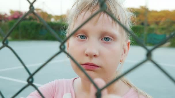 Müdes Kind blickt durch das Gitternetz des Zauns — Stockvideo