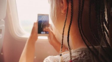 Çocuk tatilden dönüyor. Uçağın camından akıllı telefonuyla fotoğraf çekiyor. Afrika örgüleri kafalarına örülmüş.
