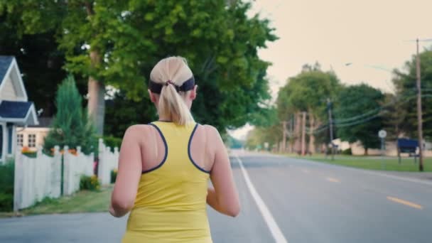 Een jonge vrouw jogt langs een typische Amerikaanse buitenwijk — Stockvideo