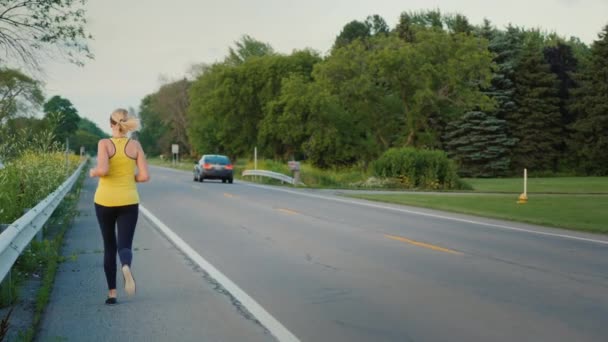 Kobieta w średnim wieku biegnie wzdłuż drogi w typowym przedmieściu Stanów Zjednoczonych, zdrowego stylu życia — Wideo stockowe