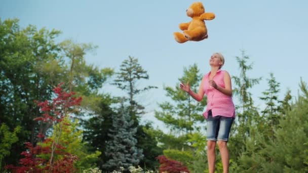Frau mittleren Alters hat Spaß wie ein Kind - sie springt auf einem Trampolin und wirft einen Teddybär in die Höhe. Aktive Menschen — Stockvideo
