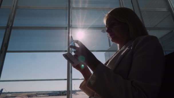 Un pasajero con una tarjeta de embarque en sus manos está de pie en una gran ventana de la terminal del aeropuerto — Vídeo de stock