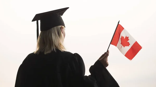 Vista trasera de un graduado con la bandera de Canadá en la mano. Estudio en canada — Foto de Stock