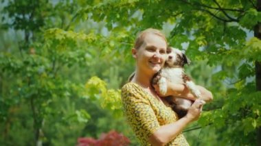 Mutlu orta yaşlı kadın ıslak köpek yavrusu kucaklar. Yağmurda bahçede duruyorlar. Hayatın unutulmaz anları