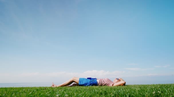 Happy barefoot woman lies on the green grass, looks at the sky and the birds flying around — Stock Video