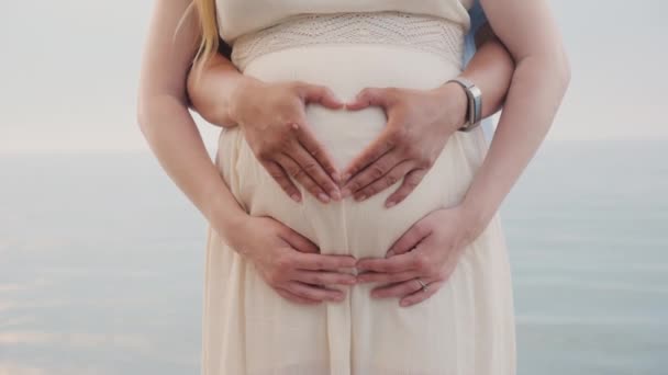 Egy fiatal pár szívet mutat egy terhes nő hasán. — Stock videók