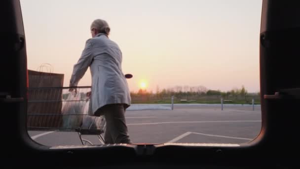 Vrouw zet boodschappentassen in de kofferbak van een auto. Brede lens shot — Stockvideo