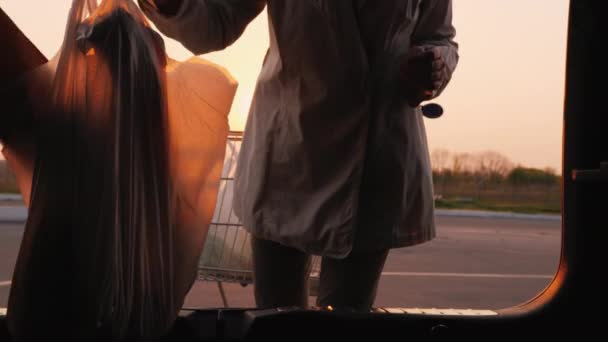 Молодая женщина кладет сумки в багажник машины — стоковое видео